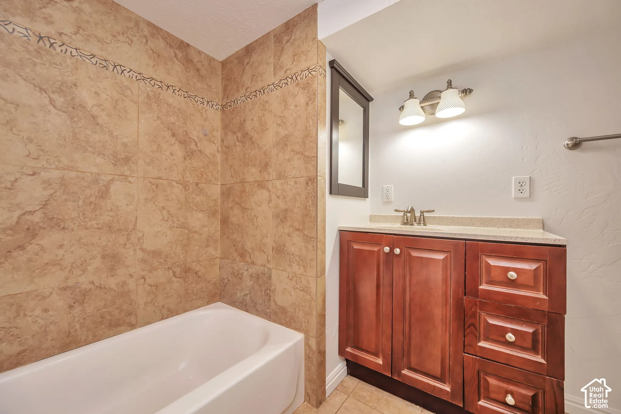 Full bathroom featuring a built-in tub, tiled shower surround with decorative accent, wood-finish vanity with countertop, and an integrated sink
