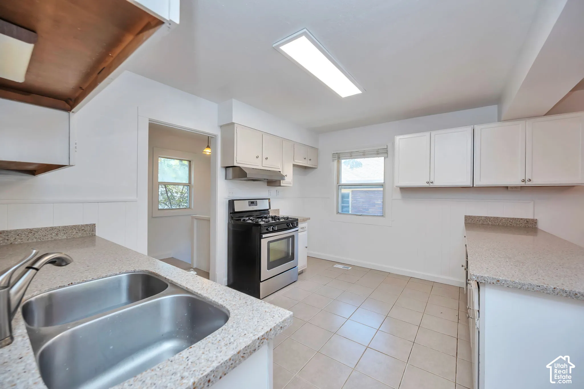 Galley kitchen featuring a dual basin stainless steel sink, quartz countertops, white cabinetry, and tile flooring