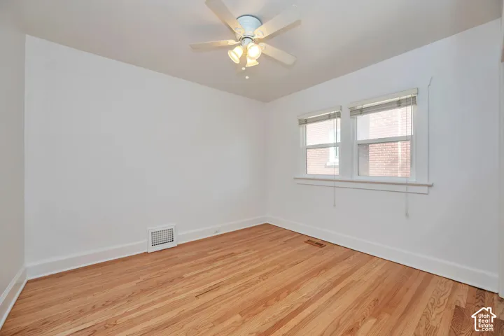 Upstairs bedroom with hardwood flooring, newly painted walls, white trim, dual windows, and ceiling fan with light fixture