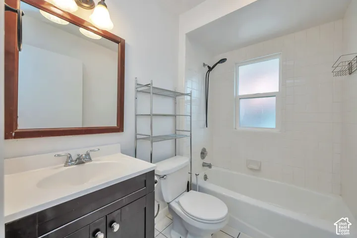 Upstairs main bathroom with tile flooring, dark wood-finish vanity with integrated sink, white tile shower surround, and a frosted window