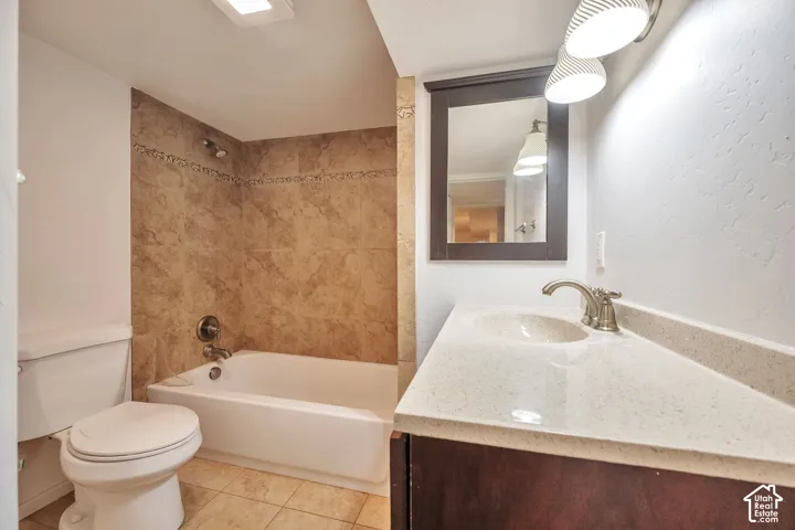 Bathroom featuring a built-in tub with tile surround, tile flooring, a single vanity with an integrated sink, and a framed mirror