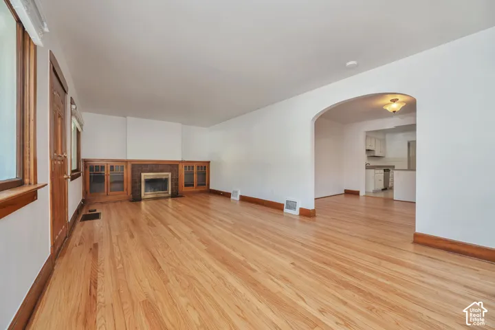 Hardwood flooring, fireplace with wood surround and built-in cabinetry, with arched entryway to dining room.
