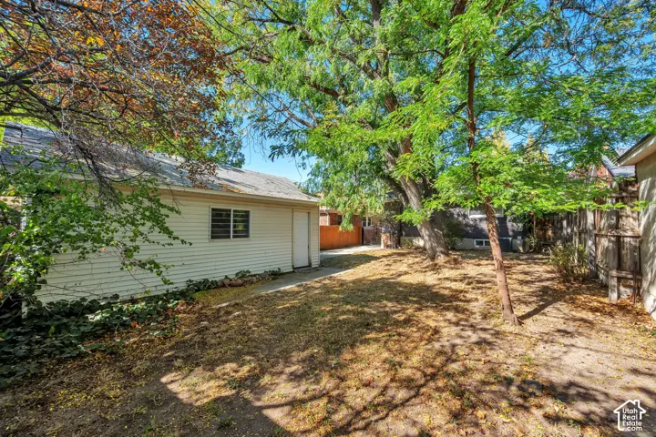 Detached garage with siding exterior and a side entry door, set within a yard featuring mature trees and wood fence
