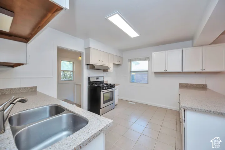 Galley kitchen featuring a dual basin stainless steel sink, quartz countertops, white cabinetry, and tile flooring