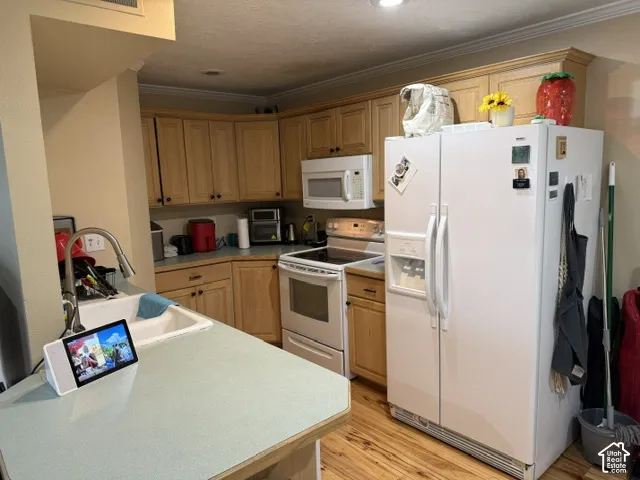 Bright, well-appointed kitchen featuring white side-by-side refrigerator, stainless steel electric range and microwave, wood-finish cabinetry, light-colored countertops, and wood-finish flooring throughout