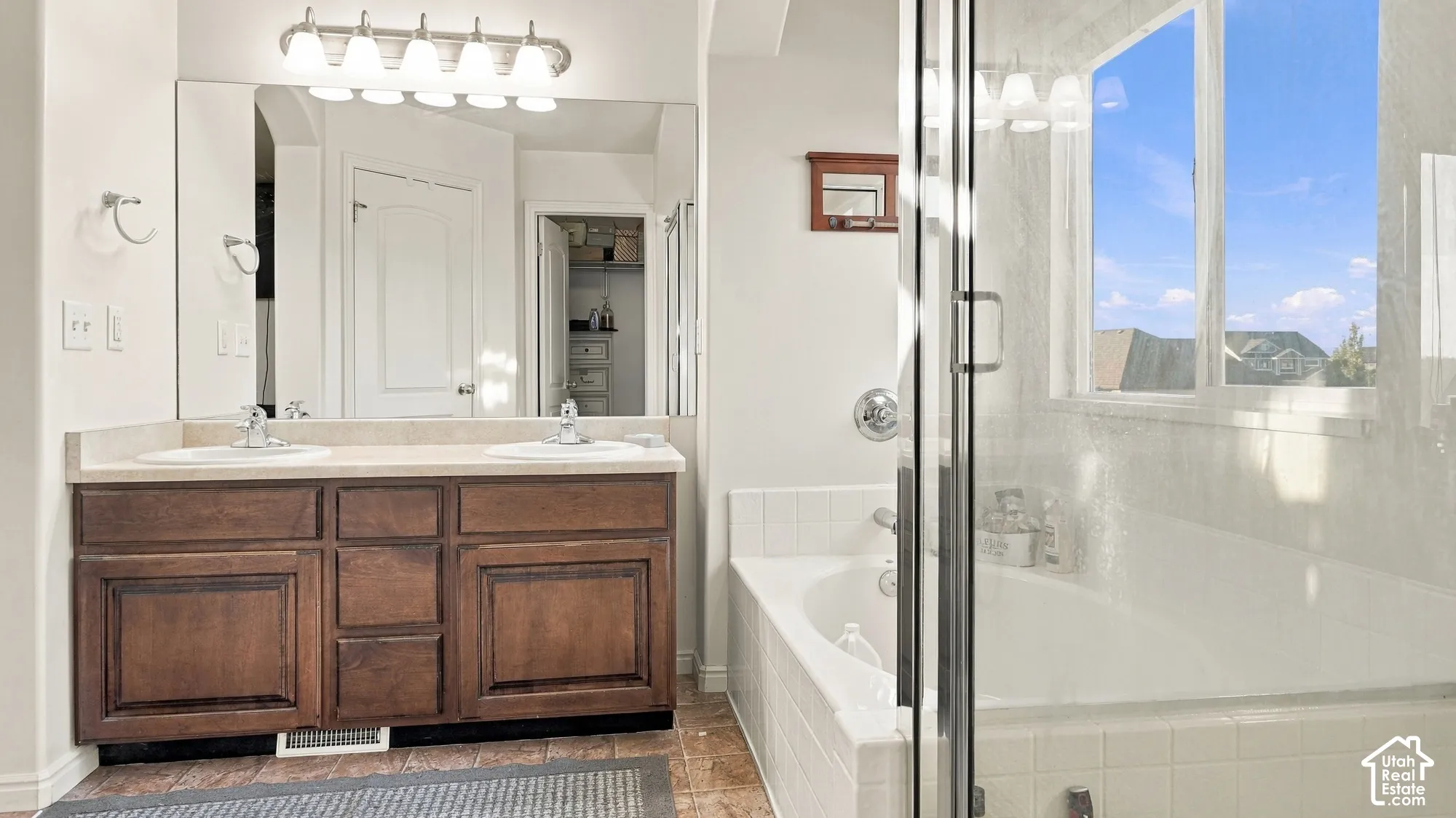 Dual vanity with wood-finish cabinetry, a large mirror, and a five-light fixture