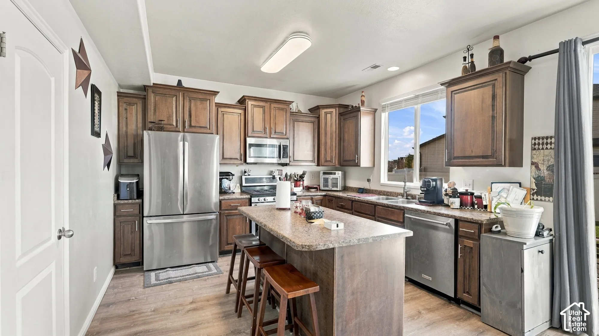 Kitchen featuring wood-finish flooring, dark wood cabinetry, a center island with seating, stainless steel appliances, and a window above the sink