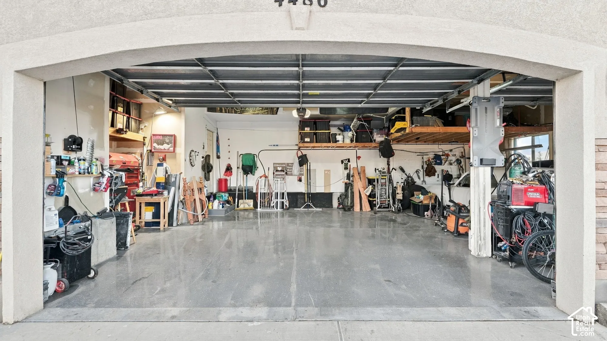 Spacious garage with an arched entryway, finished concrete flooring, and built-in overhead storage