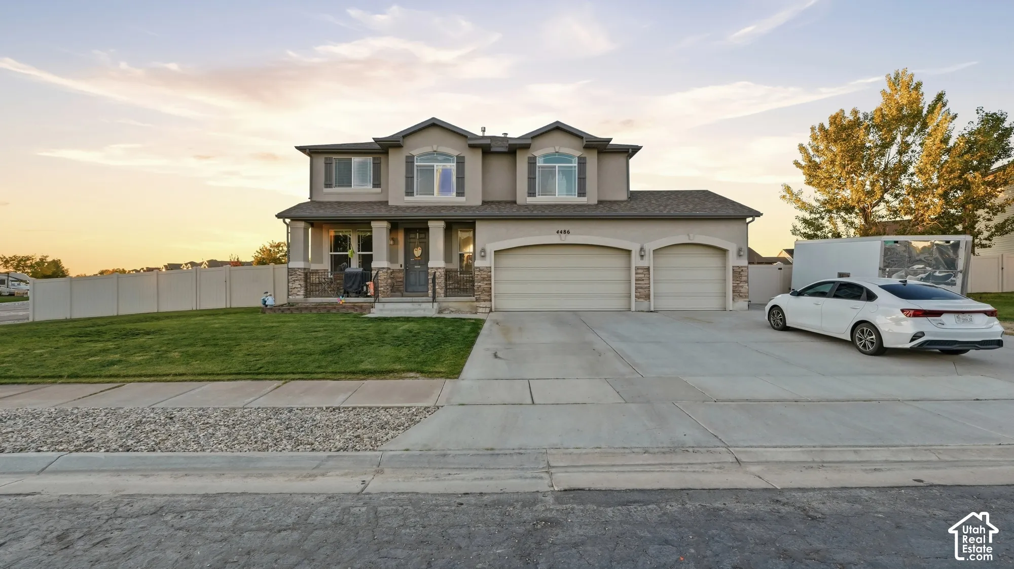 Stucco exterior with stone accents, covered front porch, two-car garage, manicured lawn, and a paved driveway