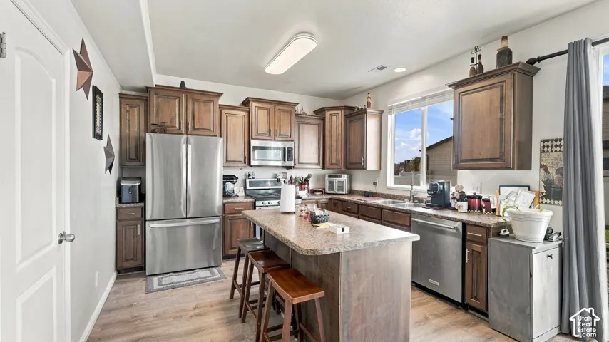Kitchen featuring wood-finish flooring, dark wood cabinetry, a center island with seating, stainless steel appliances, and a window above the sink