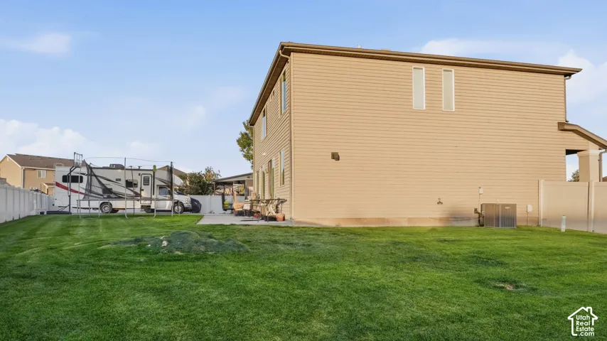 Expansive grassy yard with a concrete patio, vinyl fencing, and a two-story exterior