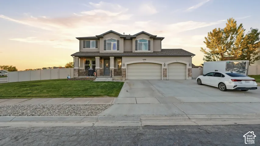 Stucco exterior with stone accents, covered front porch, two-car garage, manicured lawn, and a paved driveway