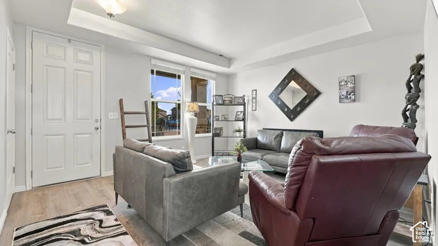 Living area featuring wood-finish flooring, a white paneled entry door, and a tray ceiling with a flush-mount light fixture