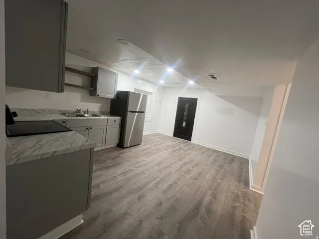 Modern open-concept kitchen and living area featuring stainless steel appliances, gray cabinetry with white countertops, wood-finish flooring throughout, and recessed ceiling lighting