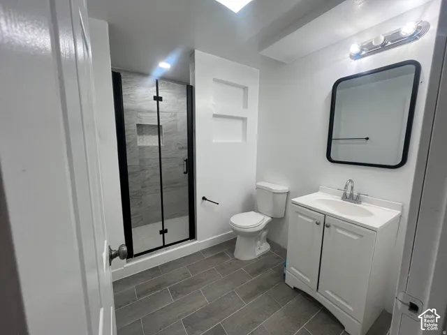 Enclosed shower with black frame, built-in shelving, vanity with integrated sink, rectangular mirror with black frame, and gray wood-finish flooring