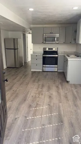 Kitchen featuring stainless steel appliances, light gray cabinetry, and wood-finish flooring