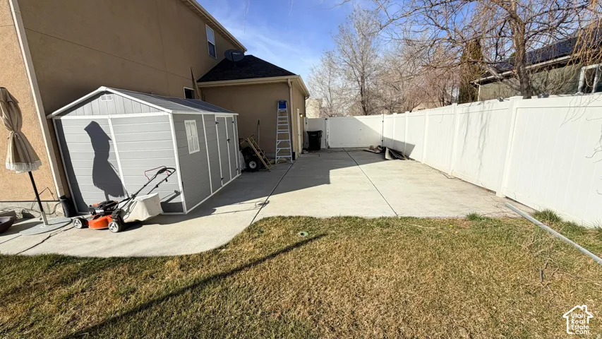 Expansive concrete patio with a detached storage shed, enclosed by a white privacy fence