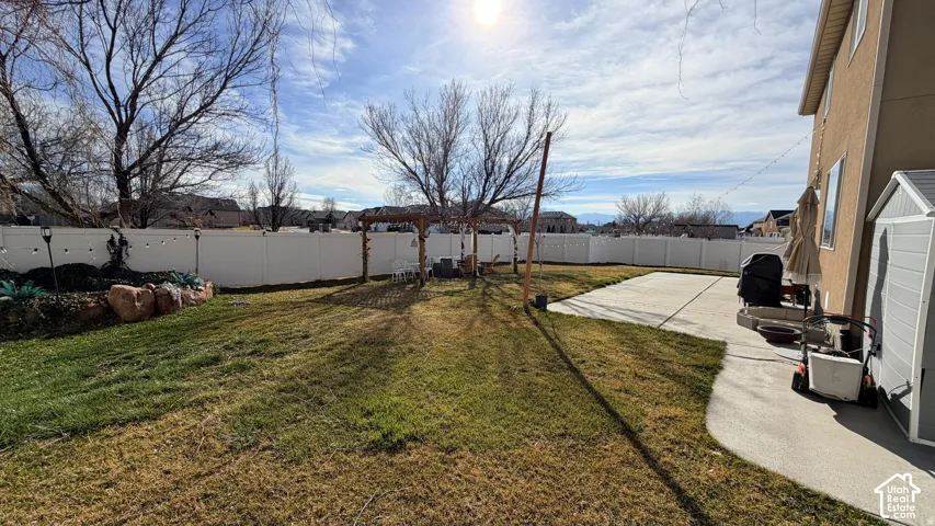 Expansive backyard featuring a privacy fence, concrete patio, lawn area, and a pergola structure