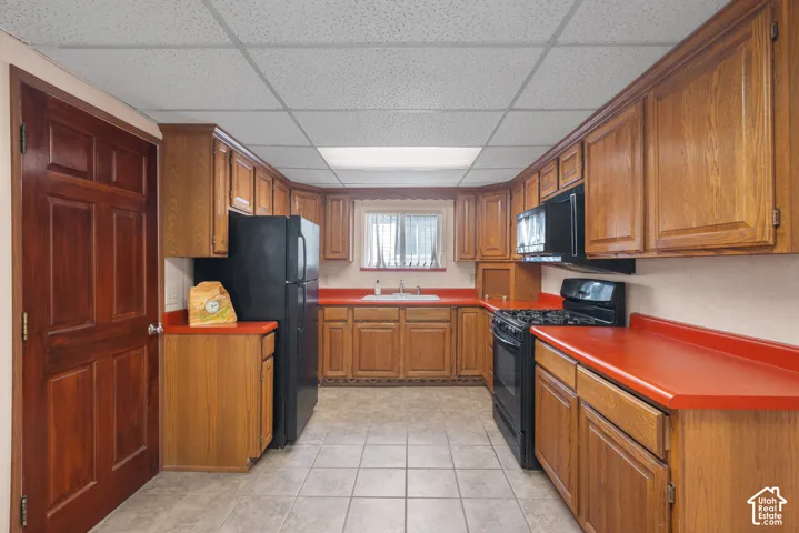 Kitchen featuring wood-finish cabinetry, solid surface countertops, tile flooring, and a drop ceiling