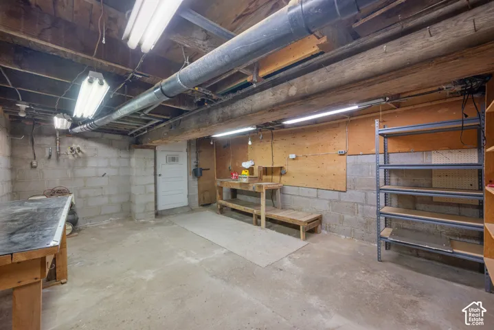 Concrete block walls, exposed wood ceiling beams, overhead fluorescent lighting, concrete flooring, and an interior door