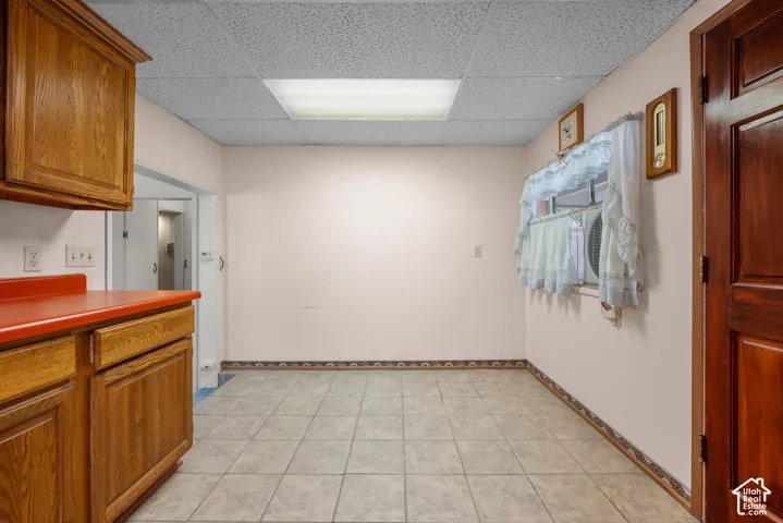 Tile flooring, wood cabinetry, red countertops, suspended acoustic ceiling, and a window with a built-in air conditioning unit