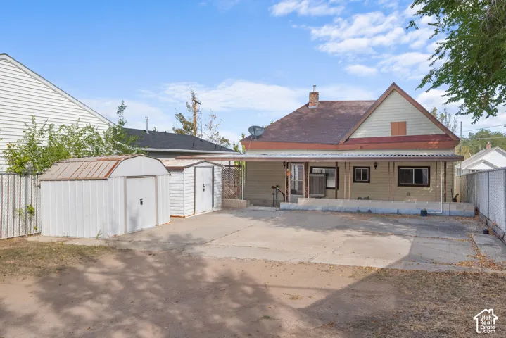 Rear exterior featuring a covered porch, multiple storage sheds, and a paved area