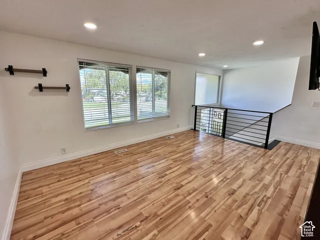 Wood-finish flooring with white baseboards, recessed lighting, and a contemporary black metal railing