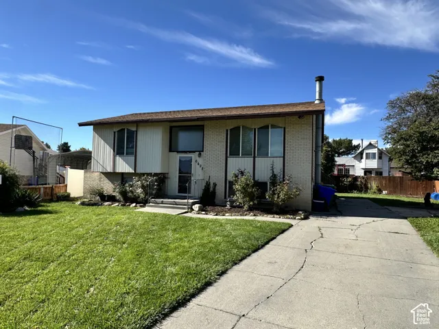 Split-level residence featuring a brick and siding exterior, front lawn, mature shrubs, and a paved driveway