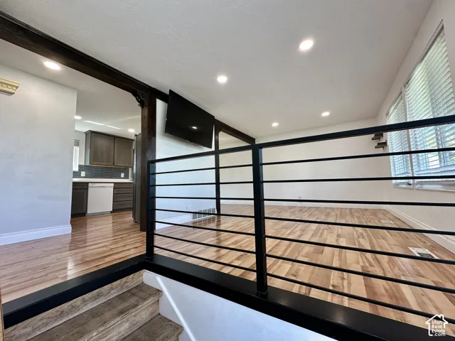 Hardwood flooring, recessed lighting, modern horizontal railing, window blinds, and wood-toned cabinetry