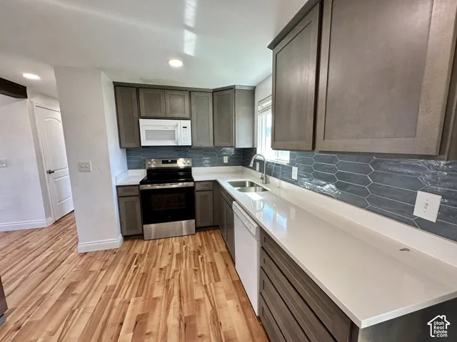 Kitchen featuring wood-finish flooring, shaker-style cabinetry, a tile backsplash, and solid surface countertops