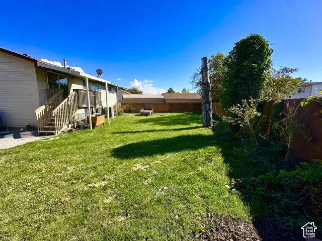 Expansive backyard with a manicured lawn, wood fencing, and a built-in wood deck with stairs