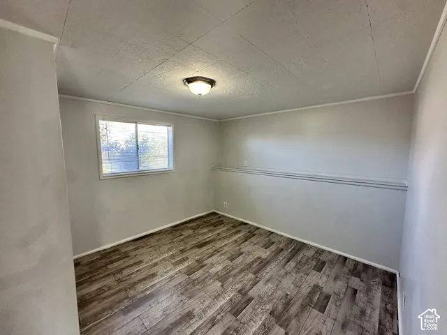 Wood-finish flooring with baseboard trim, wall-mounted light fixture, and a window with blinds