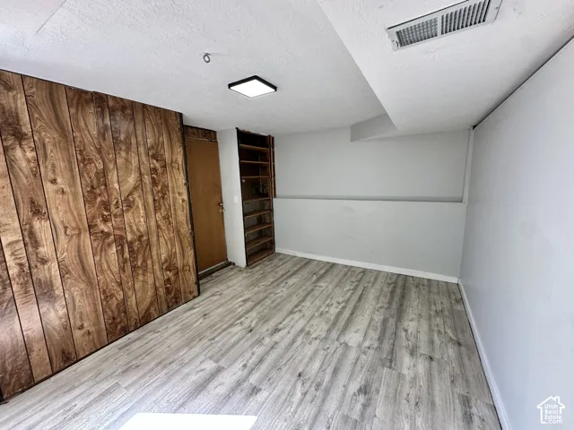 Wood-finish flooring, wood paneling, built-in shelving, flush-mount ceiling light, and a solid core door