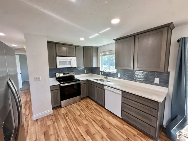 Kitchen featuring wood-finish flooring, gray cabinetry, white countertops, and a blue tile backsplash