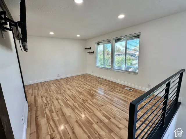 Recessed ceiling lighting, light wood-finish flooring, white painted walls, and a black metal railing