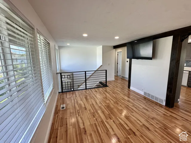 Hardwood flooring, recessed lighting, horizontal bar railing, white window blinds, and exposed wood beam accents