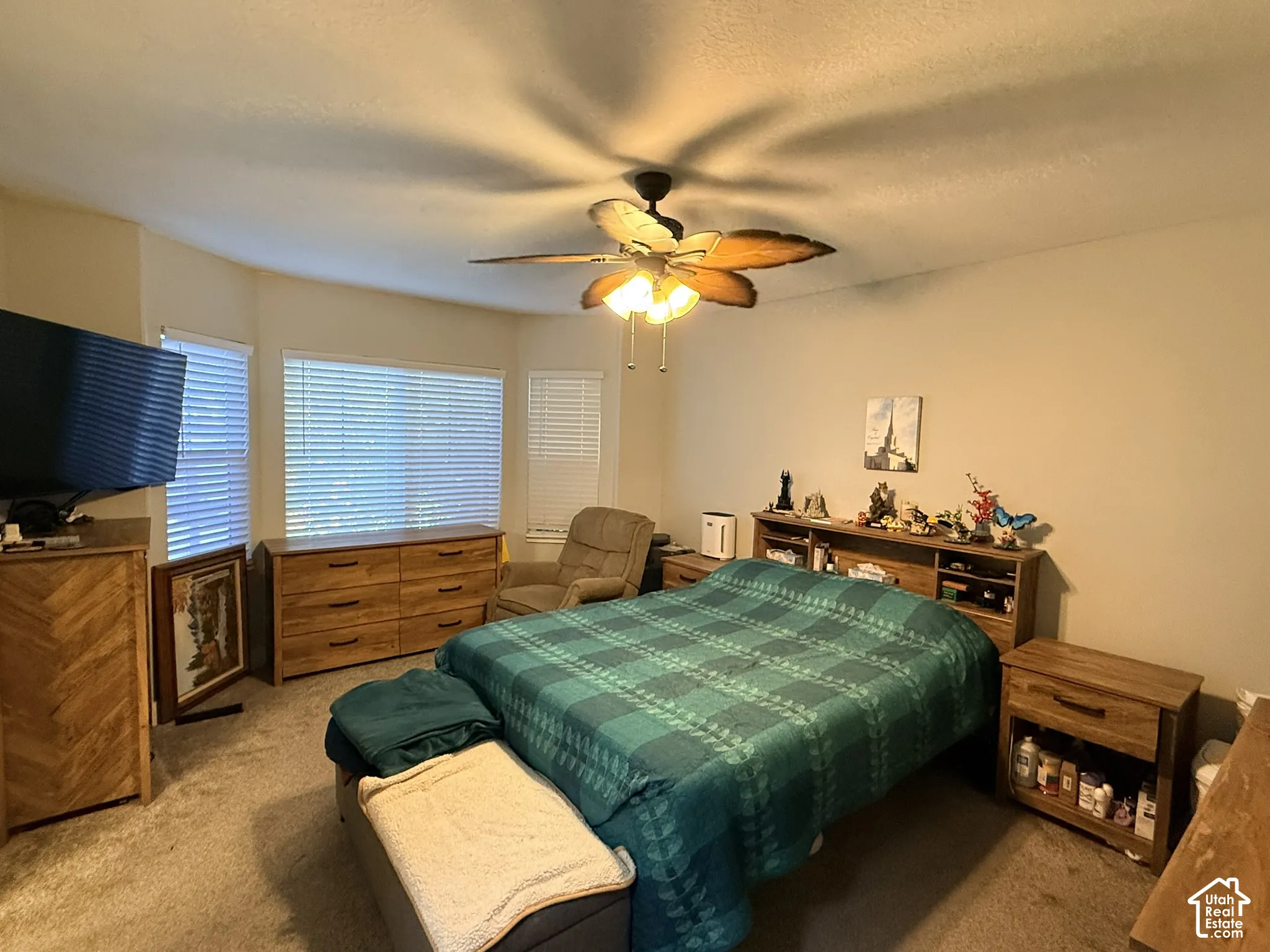 Recessed bay window with horizontal blinds, ceiling fan with integrated lighting, and carpeted flooring