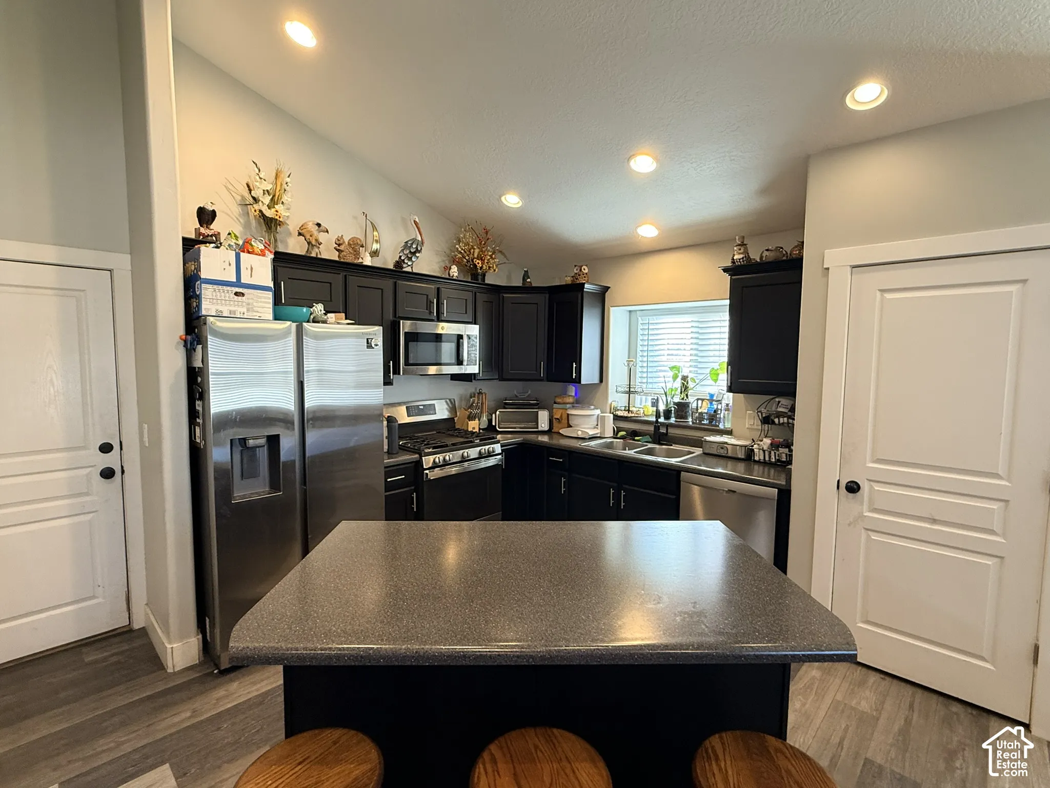 Kitchen featuring dark cabinetry, stainless steel appliances, a center island with seating, and wood-finish flooring