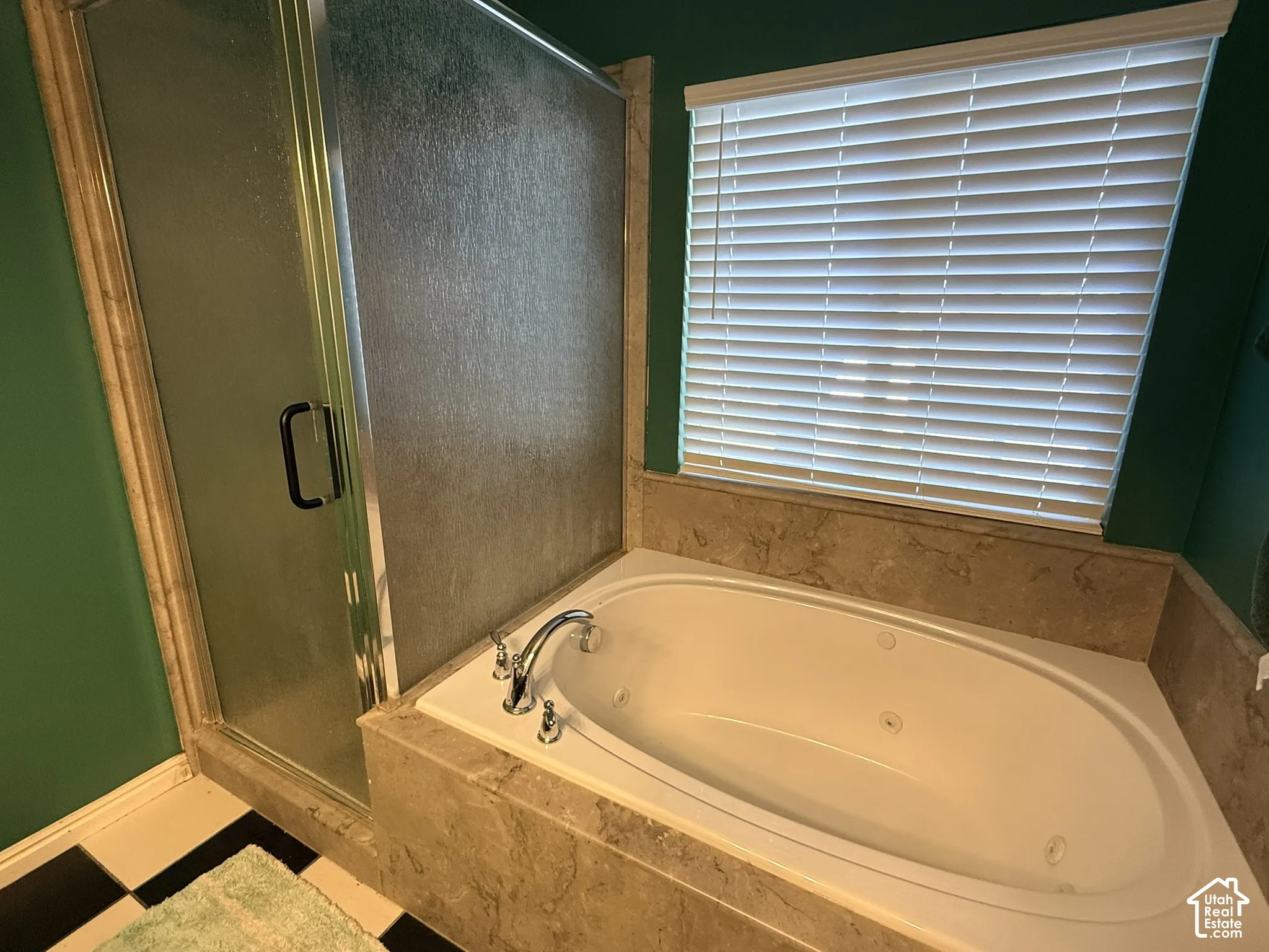 Built-in jetted tub surrounded by stone-look tile, glass-enclosed shower, and checkered floor tile