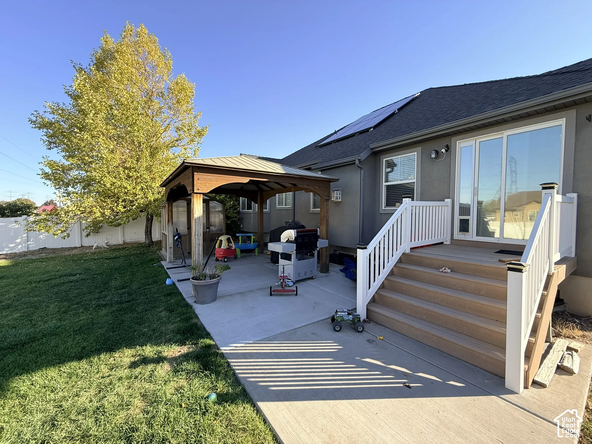 Expansive concrete patio with a wooden gazebo, composite deck with white railings, and a sliding glass door