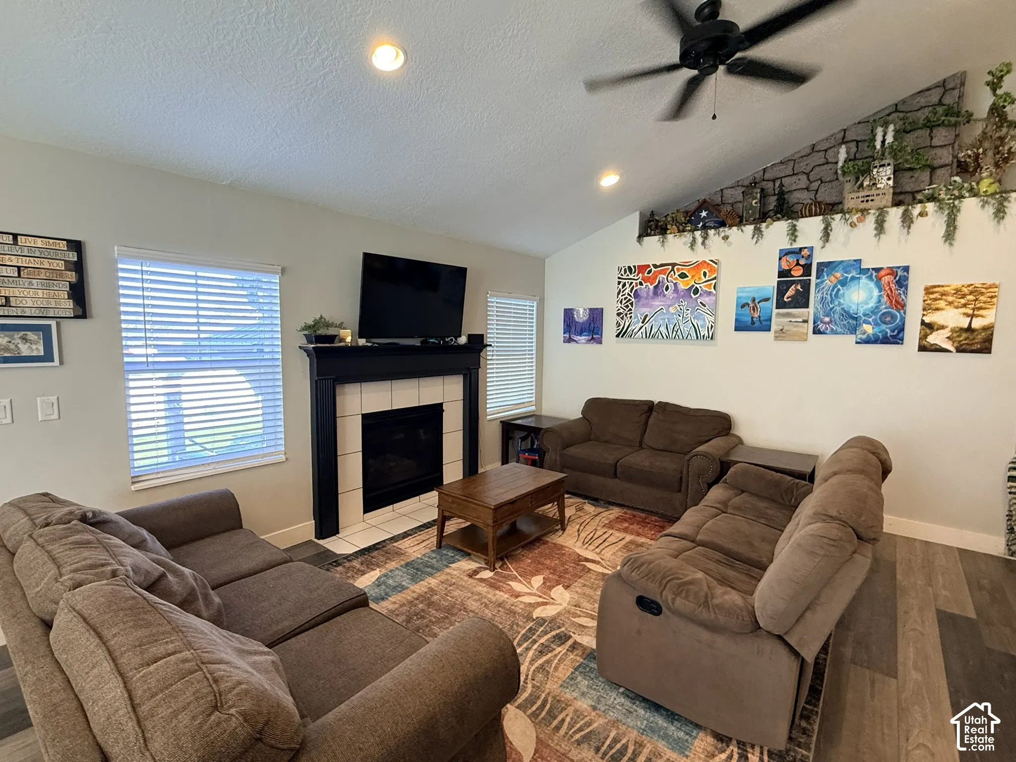 Vaulted ceiling with a ceiling fan, fireplace with white tile surround and dark mantel, and wood-finish flooring