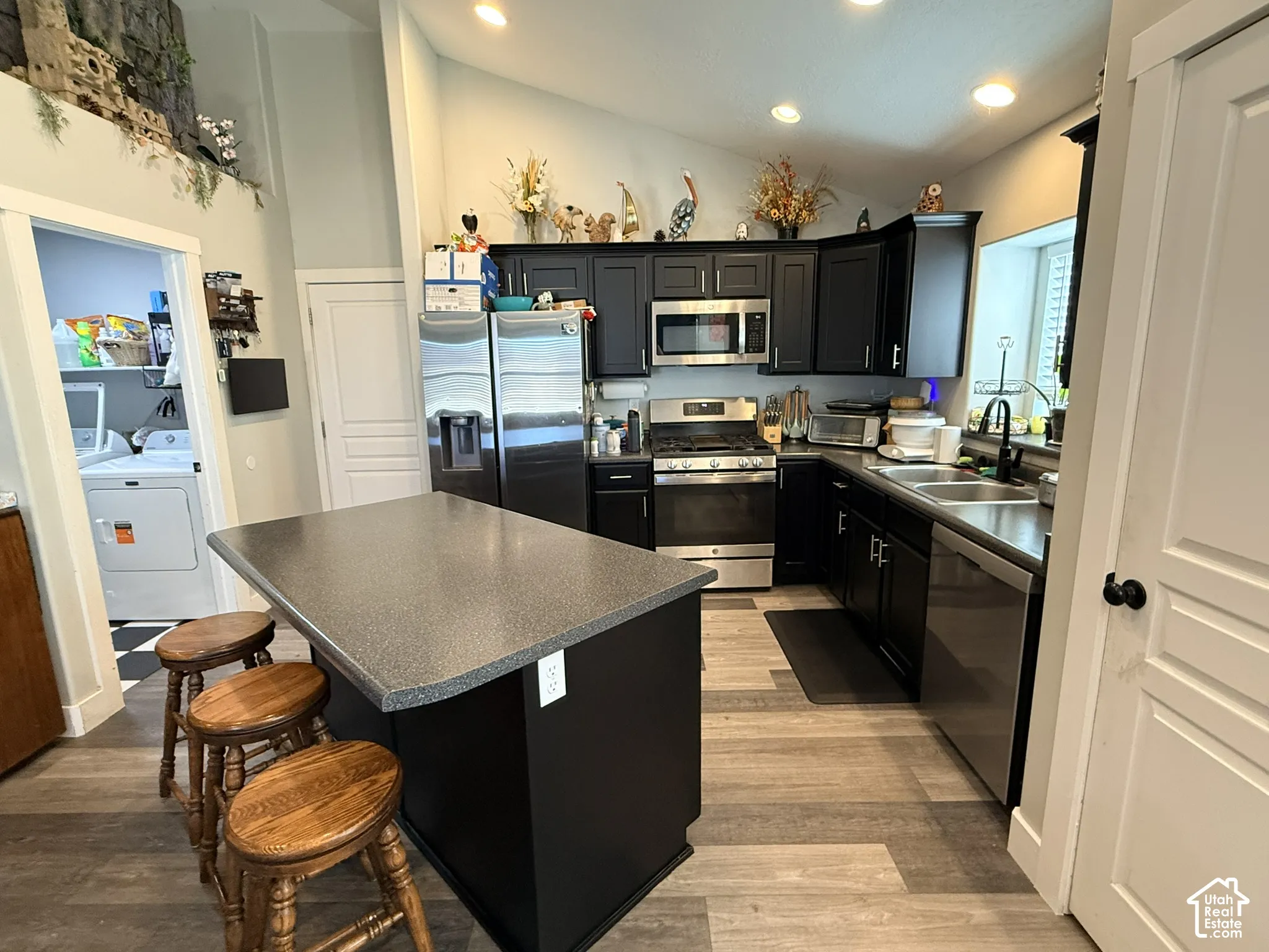 Kitchen featuring dark cabinetry, stainless steel appliances, a center island with seating, wood-finish flooring, and recessed lighting