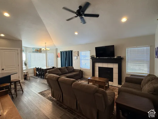 Vaulted ceilings with recessed lighting, ceiling fan, fireplace with white tile surround and dark mantle, and wood-finish flooring