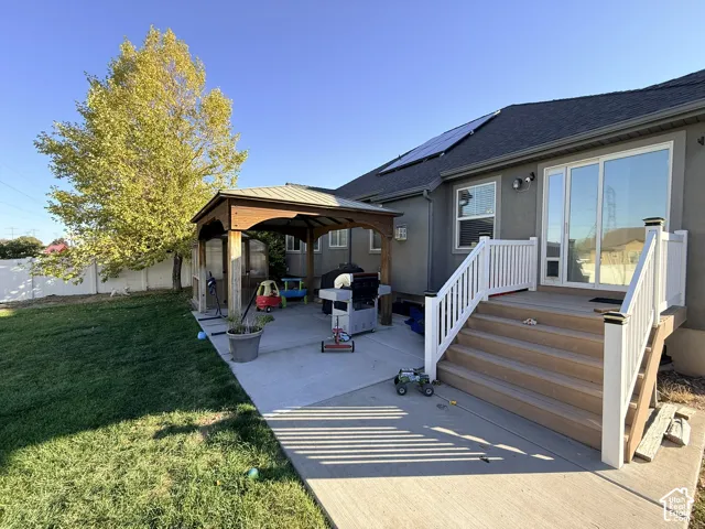 Expansive concrete patio with a wooden gazebo, composite deck with white railings, and a sliding glass door