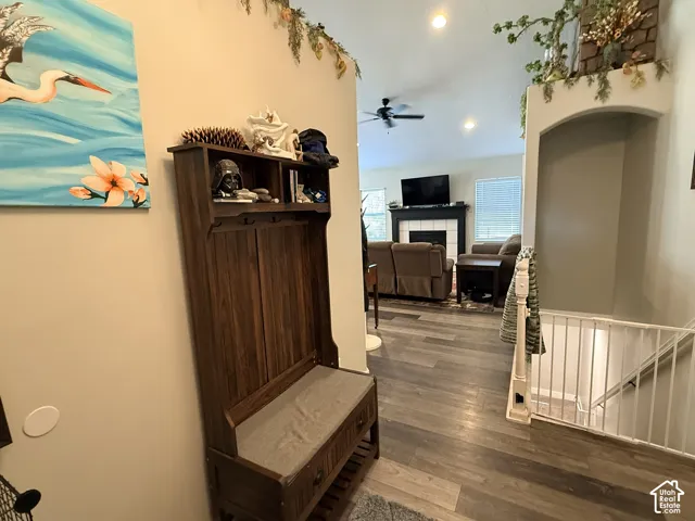 Wood-finish flooring, recessed lighting, white fireplace surround with dark mantel, ceiling fan, and staircase with white railing