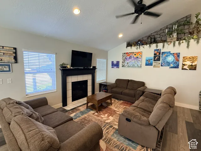 Vaulted ceiling with a ceiling fan, fireplace with white tile surround and dark mantel, and wood-finish flooring