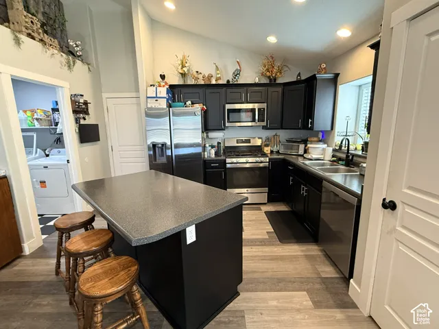 Kitchen featuring dark cabinetry, stainless steel appliances, a center island with seating, wood-finish flooring, and recessed lighting