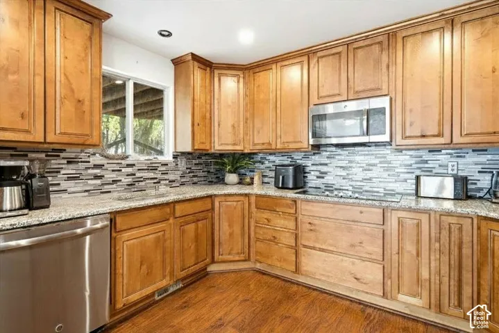 Wood-finish flooring, custom wood cabinetry, stainless steel appliances, granite countertops, and a mosaic tile backsplash
