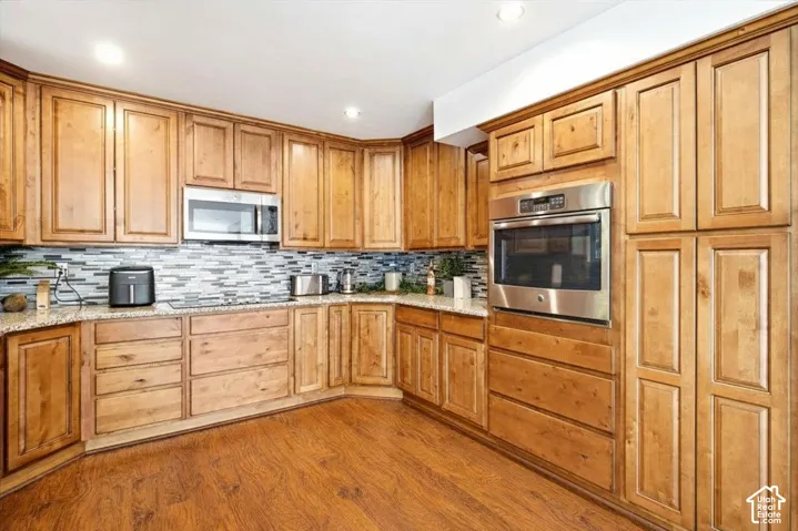 Wood-finish flooring with extensive wood cabinetry, granite countertops, and a mosaic tile backsplash