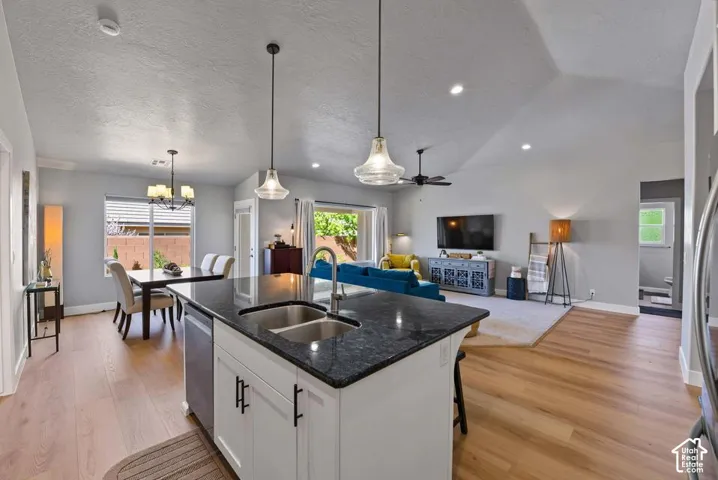 Kitchen island with dual basin sink and dark countertop, wood-finish flooring, vaulted ceiling, recessed lighting, and a dining area with a chandelier